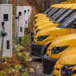 Row of yellow electric vans charging at stations