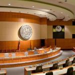 Bernie’s AI Grab Sparks Panic Interior view of a government chamber with wooden paneling and seating
