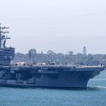 Pentagon’s Cuba Standoff – Is a Strike Inevitable? Aircraft carrier escorted by a tugboat in a harbor