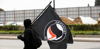 Antifa Threatens ANARCHY as Attacks on Alternative for Germany (AfD) Mount Hooded person carrying a large black flag on a city street