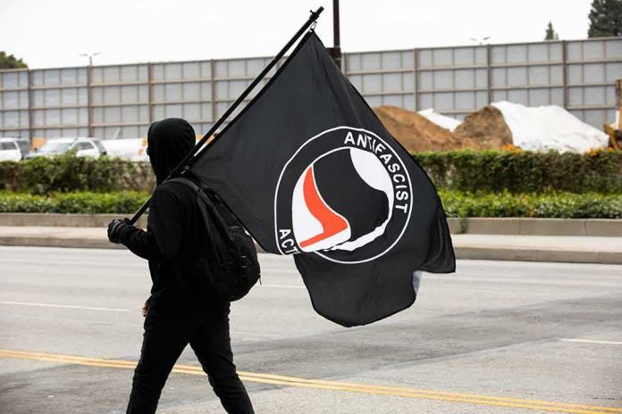 Hooded person carrying a large black flag on a city street