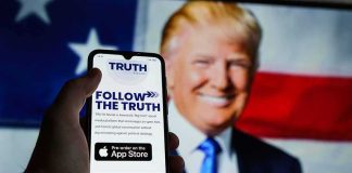 Smartphone showing Truth Social app screen with Donald Trump on a U.S. flag backdrop