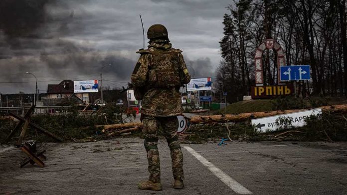 Soldier in camouflage stands at roadblock with smoke in the distance