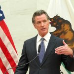 Gavin Newsom speaks at a podium with U.S. and California flags behind him