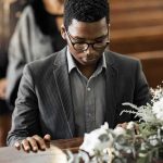 Man in suit at a funeral touching a casket with flowers
