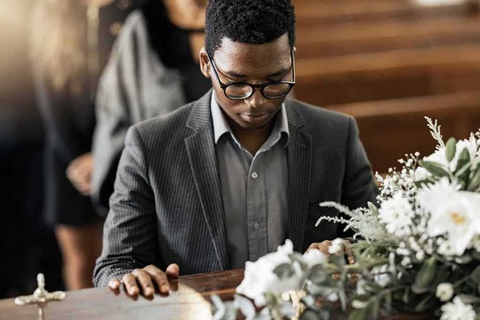Man in suit at a funeral touching a casket with flowers