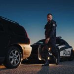 Police officer standing near patrol car during twilight traffic stop