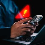 hands holding smartphone with warning alert icon