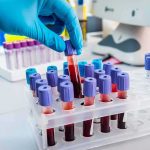 Gloved hand holding a blood sample tube in a lab rack
