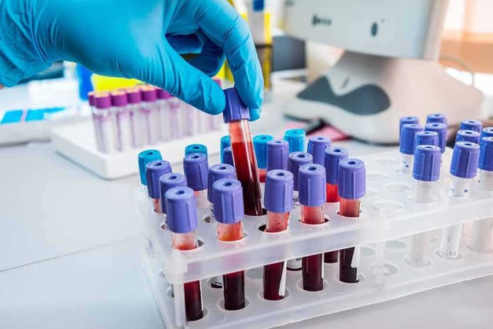 Gloved hand holding a blood sample tube in a lab rack