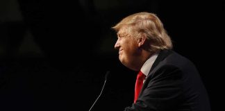 Donald Trump speaking at a podium in profile against a dark background