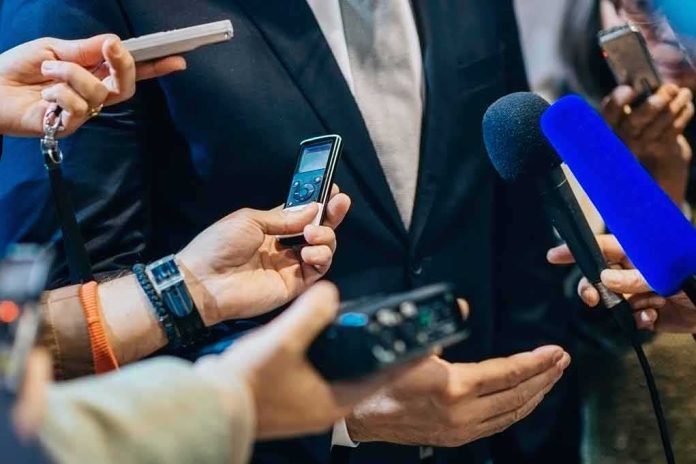 shutterstock_471987556 businessperson in suit surrounded by microphones and recorders