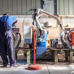 Factory worker operates near an industrial robot arm in a workshop