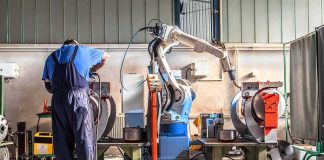 Factory worker operates near an industrial robot arm in a workshop