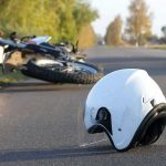 White motorcycle helmet on road with fallen bike in background