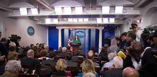 Press secretary at podium addressing reporters in briefing room