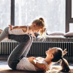 Mother and daughter doing airplane pose together at home