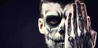 Person with skull face paint covering one eye with a skeleton-painted hand