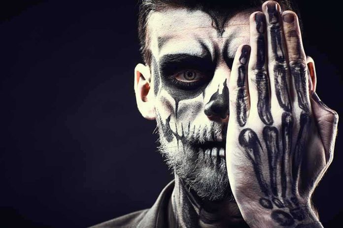 Person with skull face paint covering one eye with a skeleton-painted hand