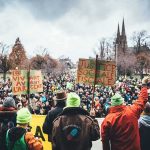 Christian Jones at a large outdoor protest with crowds and handmade signs