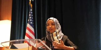 Federal Agents RAID Ilhan Omar’s Home Ilhan Omar speaking at a podium with a microphone