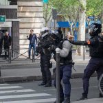 Riot police in helmets line a city street during an operation