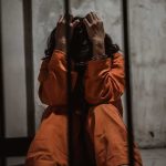 Prisoner in orange jumpsuit sitting behind bars