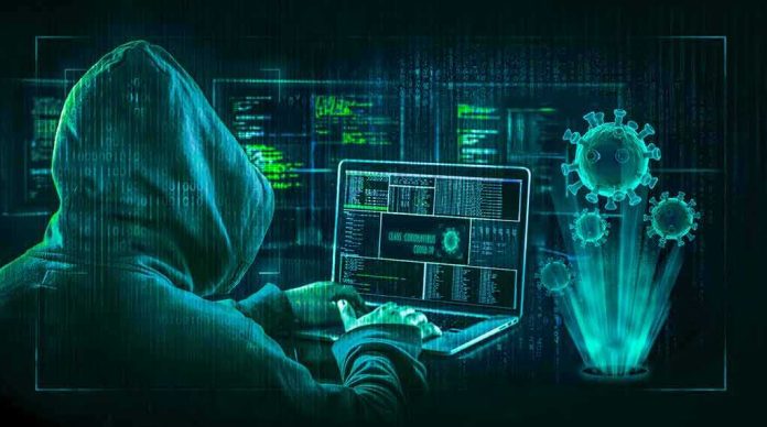 shutterstock_1704713953 Hacker in hoodie using laptop with digital virus graphics