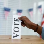 Hand placing a ballot into a wooden ballot box