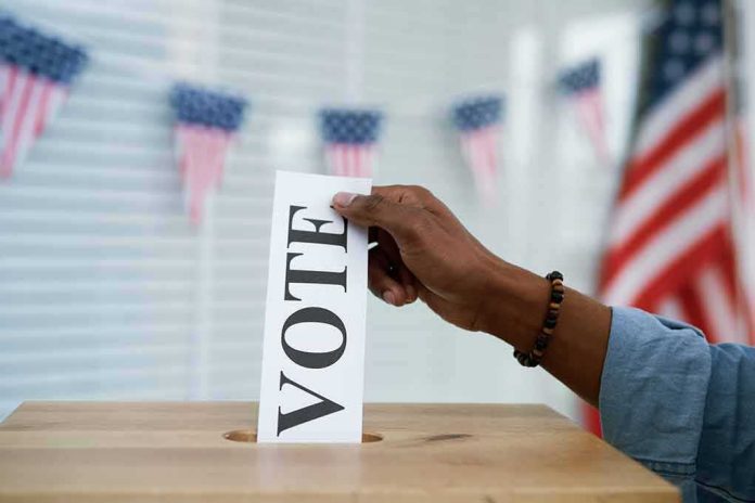 shutterstock_1837117150 Hand placing a ballot into a wooden ballot box