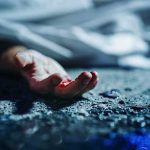 Human hand on gritty ground near a covered body
