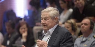 George Soros speaks with a microphone; Viola Odebrecht is seated in the audience