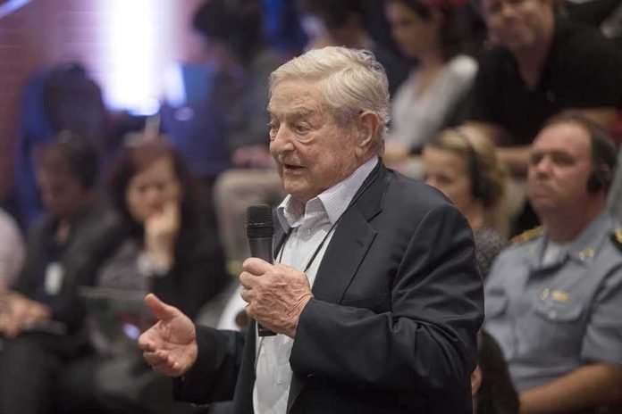 George Soros speaks with a microphone; Viola Odebrecht is seated in the audience