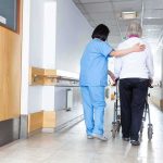 Nurse assisting an elderly person with a walker in a hallway