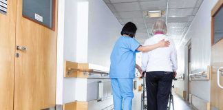 Nurse assisting an elderly person with a walker in a hallway