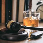 Judge's gavel with car key and whiskey glass on desk