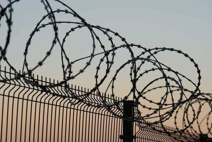 shutterstock_771028372 Razor wire coils atop a metal security fence at dusk